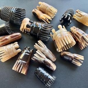 Puede incluir: Una colección de accesorios para el cabello, que incluye pinzas y peines, en varios colores y patrones. Las pinzas y peines están hechos de materiales como cuerno y plástico, con tonos de negro, marrón y beige. Las pinzas tienen un diseño único.