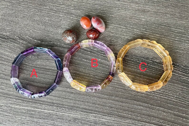 May include: Three bracelets made of faceted gemstone beads. The bracelets are labelled A, B, and C. Bracelet A is purple, blue, and green. Bracelet B is yellow, orange, and purple. Bracelet C is yellow.