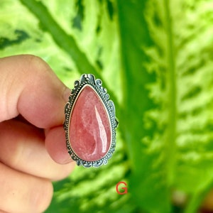 May include: A silver ring with a pink teardrop-shaped gemstone set in a detailed filigree design.