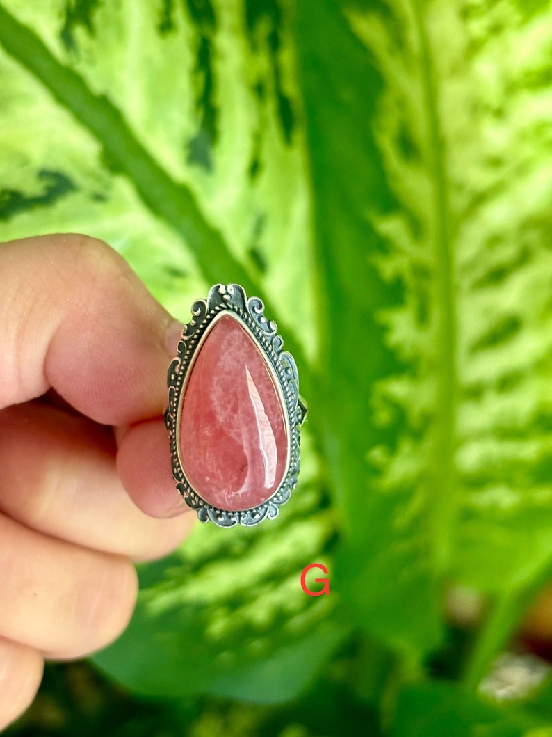 May include: A silver ring with a pink teardrop-shaped gemstone set in a detailed filigree design.
