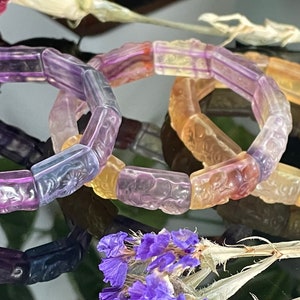 May include: Three colourful bracelets made of faceted glass beads. The beads are carved with intricate designs and feature a gradient of purple, pink, and yellow.