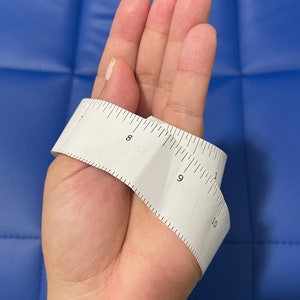 May include: A white measuring tape wrapped around a hand, showing measurements from 7 to 10 inches.