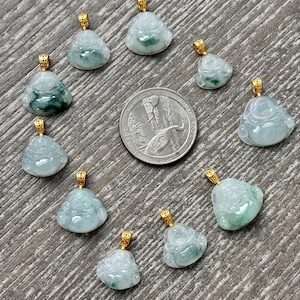 May include: A collection of jade Buddha pendants with gold-colored bails. The pendants are various shades of green and white, with intricate carved details. A US quarter is in the center of the pendants.