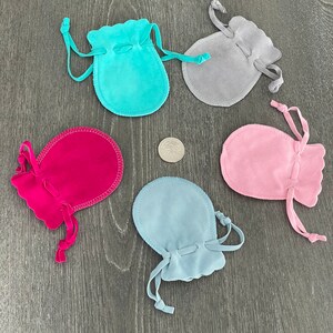 Puede incluir: Cinco peque&ntilde;as bolsas de cord&oacute;n en diferentes colores: turquesa, gris, rosa, azul claro y rojo. Las bolsas est&aacute;n hechas de un material suave y aterciopelado y tienen un borde festoneado.