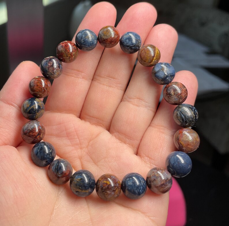 May include: A bracelet made of round, multi-colored beads with a tiger's eye pattern. The beads are a mix of blue, brown, and gold.