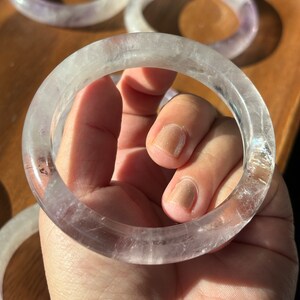May include: A clear, translucent amethyst bangle bracelet with a light purple hue. The bracelet is made of natural stone and has a smooth, polished finish.