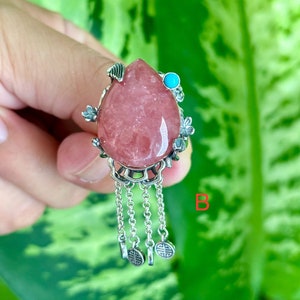 May include: A pink gemstone pendant with silver floral accents and a turquoise stone. The pendant has a chain with four charms.