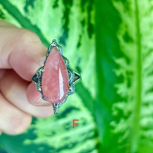 May include: A silver ring with a pink teardrop-shaped gemstone set in a delicate filigree design.