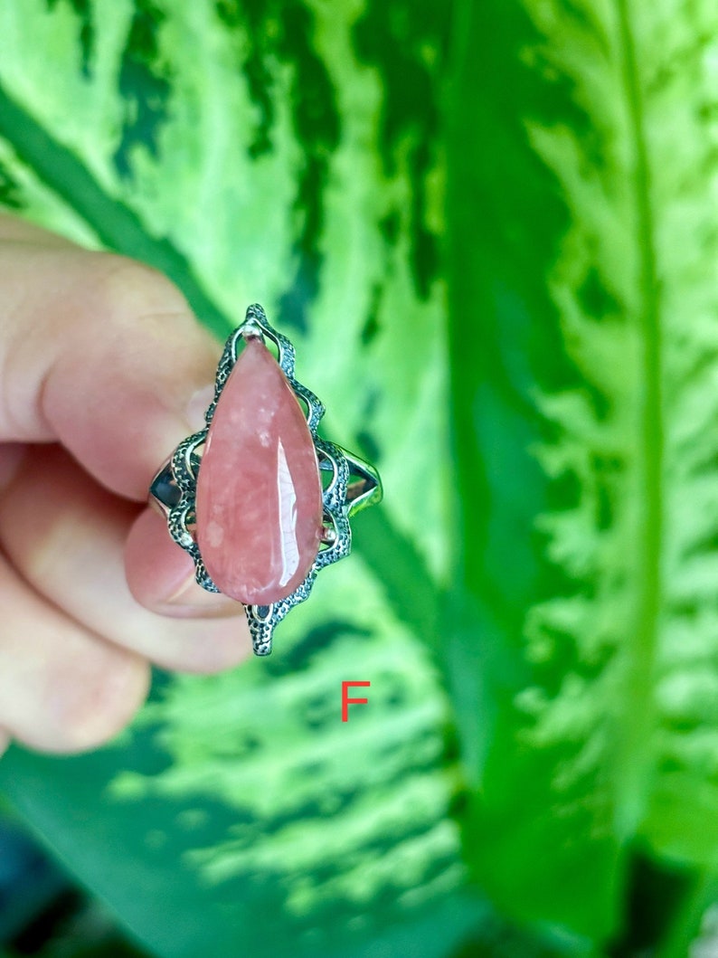 May include: A silver ring with a pink teardrop-shaped gemstone set in a delicate filigree design.