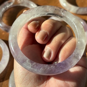 May include: A set of amethyst crystal bracelets. The bracelets are a light purple color and have a smooth, polished finish. They are stacked on top of each other, creating a beautiful display.