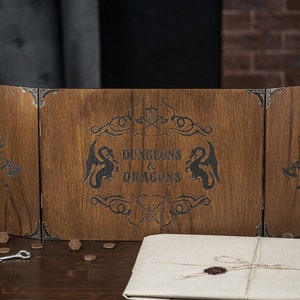 Może przedstawiać: Drewniany ekran do gry Dungeons & Dragons z grawerowanymi grafikami. Ekran jest brązowy z metalowymi narożnikami i zawiera napis "DUNGEONS & DRAGONS" wraz z wizerunkami smoków i wikingów. Klucz i monety leżą na stole.