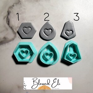 Könnte beinhalten: Drei Sätze Polymer Clay Cutter, jeder mit einer anderen Form: ein Hexagon, eine Teardrop und eine geometrische Form. Die Cutter sind in zwei Farben: Grau und Türkis. Die Cutter sind in drei Reihen angeordnet, wobei die grauen Cutter oben und die türkisfarbenen Cutter unten liegen. Der Text "Blessed Eli Polymer Clay Jewelry" ist am unteren Rand des Bildes sichtbar.