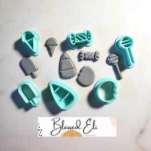 May include: A set of 10 blue plastic cookie cutters shaped like various candy and ice cream treats, including a lollipop, ice cream cone, popsicle, candy cane, and a candy bar. The cutters are arranged on a white surface.