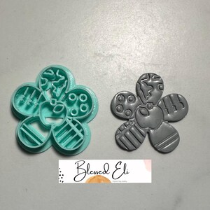 May include: Two flower-shaped polymer clay cutters. One is a bright teal colour, and the other is grey. Each petal has a different design. The cutters are for polymer clay jewellery making.