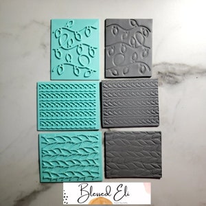 Könnte beinhalten: Sechs Silikonstempel zum Backen und Dekorieren. Zwei Stempel zeigen ein Lichterketten-Design, zwei ein Zopfmuster und zwei ein Blatt-Muster. Die Stempel sind in zwei Farben: Türkis und Grau.