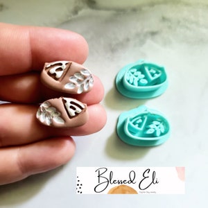 May include: Two pairs of polymer clay earrings with a white leaf design on a brown background. The earrings are shown next to their matching moulds, which are turquoise blue.