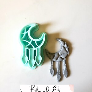 Könnte beinhalten: Zwei Traumfänger-Ohrringe aus Polymer Clay in Form eines Halbmondes. Die Ohrringe sind in hellblau und grau gehalten. Die Ohrringe sind mit "Blessed Eli Polymer Clay Jewelry" beschriftet.