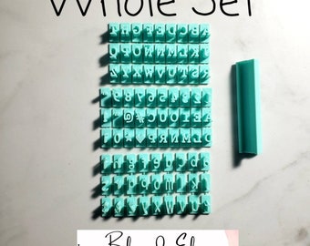 May include: A set of turquoise polymer clay stamps with the alphabet, numbers, and symbols. The stamps are arranged in rows on a white surface. The set also includes a turquoise tool for smoothing clay. The image includes the text "Whole Set" and "Blessed Eli Polymer Clay Jewelry".