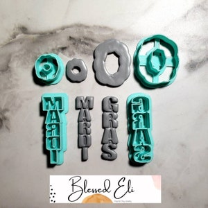 May include: Set of seven grey and turquoise plastic cookie cutters. The cutters are shaped like the words "Mardi Gras" and a donut.
