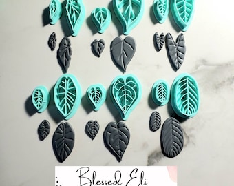 May include: A set of 14 teal green leaf-shaped cookie cutters and 7 grey leaf-shaped cookie cutters. The cookie cutters are arranged in rows on a white surface. The text "Blessed Eli Polymer Clay Jewelry" is visible at the bottom of the image.