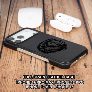 May include: Black leather iPhone case featuring a detailed lion's head design. The case is shown on a wooden surface with a laptop, a white mouse, and wireless earbuds. The text on the case reads "FULL GRAIN LEATHER CASE IPHONE 17 PRO MAX, IPHONE 17 PRO, IPHONE 17 AIR, IPHONE 17."