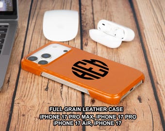 May include: An orange leather iPhone case with a black monogram design. The case is shown with a white mouse, wireless earbuds, and a laptop on a wooden surface. The text on the image reads "FULL GRAIN LEATHER CASE" and lists iPhone models.