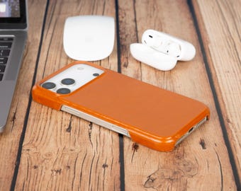 May include: A tan leather smartphone case with a rectangular cutout for the camera lenses, featuring a smooth finish and a slim profile. The case is designed to fit a mobile device, showing precise openings for the side buttons and charging port.