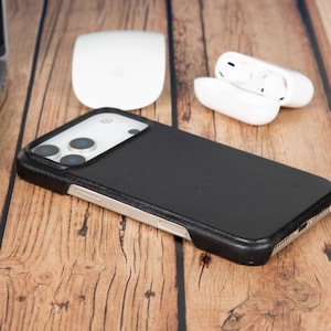Puede incluir: Una funda de smartphone negra con acabado texturizado y un recorte elevado para la cámara, con un perfil delgado que deja al descubierto los botones laterales metálicos del dispositivo. Diseñada para un teléfono con triple cámara.