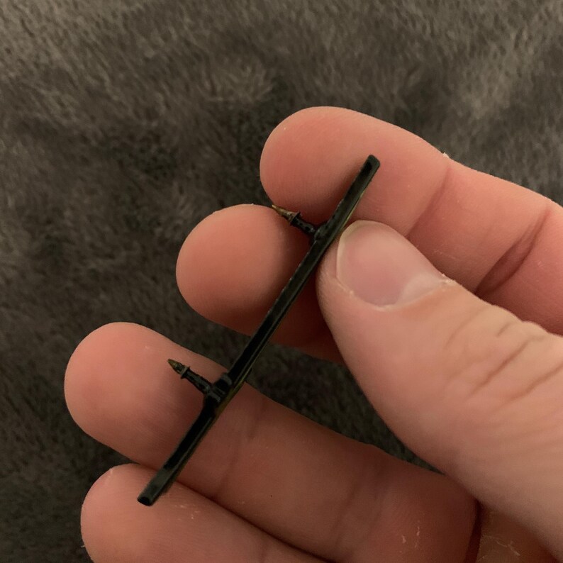 May include: A black metal bar with two small metal prongs on either end. The bar is about 5 inches long.