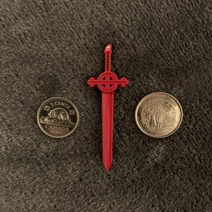 May include: A red plastic sword with a cross-shaped handle and a gold Canadian 5-cent coin from 2002.