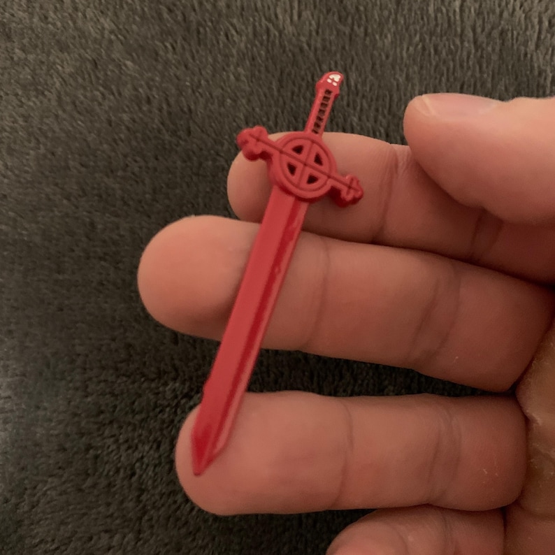 May include: A red plastic sword with a circular design on the hilt. The sword is about 4 inches long.