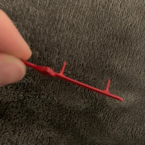 May include: A red plastic tool with four prongs, used for attaching or removing items.