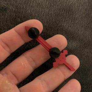 May include: Red metal pin with a skull and crossbones design. The pin has a black rubber backing for attaching to clothing or a bag.