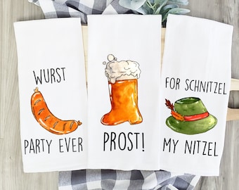 May include: Three white kitchen towels with a German theme. The first towel has a cartoon sausage and the text "Wurst Party Ever". The second towel has a cartoon beer stein and the text "Prost!". The third towel has a cartoon hat and the text "For Schnitzel My Nitzel".
