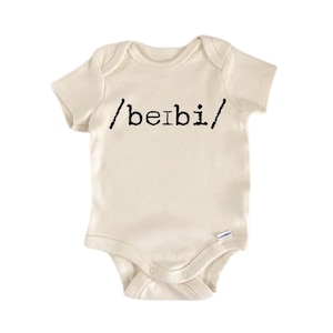 May include: Cream-colored baby bodysuit with short sleeves. The text "/beibi/" is printed in black across the front. The bodysuit has a snap closure at the bottom and a round neckline. The fabric appears to be soft and comfortable.