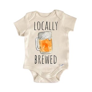Puede incluir: Un body de bebé color crema con las palabras "LOCALLY BREWED" en letras negras. Una ilustración en acuarela de una jarra de cerveza con líquido naranja y espuma blanca está centrada en la parte delantera.