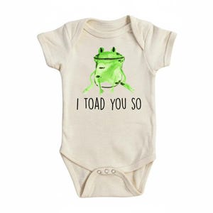 May include: A cream-coloured baby onesie featuring a green watercolour frog illustration. The frog is centered, with the text "I TOAD YOU SO" printed below in black. The onesie has short sleeves and poppers at the bottom.