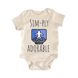 May include: A cream-colored baby onesie with the words "SIM-PLY ADORABLE" in black lettering. The onesie features a graphic of a white airplane inside a blue rectangle, with a gray and yellow design below.
