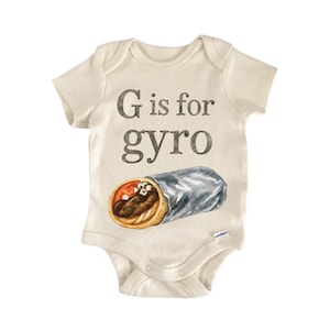 May include: A cream-colored baby onesie with the text "G is for gyro" in brown letters. Below the text is a watercolor illustration of a gyro wrap. The wrap is in a silver foil wrapper.