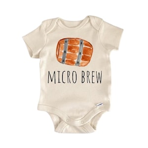 Puede incluir: Body de bebé color crema con una ilustración de acuarela de un barril marrón con bandas grises. El texto "MICRO BREW" está impreso en negro debajo. Un body de bebé lindo y divertido.