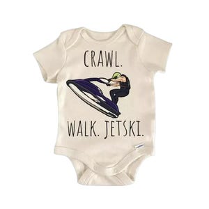 May include: A cream-coloured baby onesie featuring the text "Crawl. Walk. Jetski." in black. The graphic depicts a person on a purple and white jet ski. A fun and playful design for a baby.