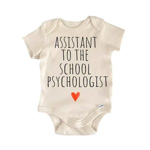 A beige baby onesie with the text "ASSISTANT TO THE SCHOOL PSYCHOLOGIST" printed on it, along with a small red heart symbol.