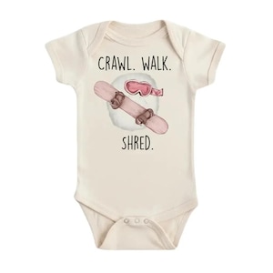Può includere: Body per neonati color crema con la scritta "Crawl. Walk. Shred." presenta un'illustrazione ad acquerello di uno snowboard, occhiali e una nuvola soffice. Lo snowboard è rosa chiaro con attacchi marroni.