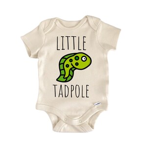 May include: Cream-colored baby bodysuit with the words "LITTLE TADPOLE" in black. A green tadpole illustration with black details is centered below the word "LITTLE". The bodysuit has short sleeves and snaps at the bottom.