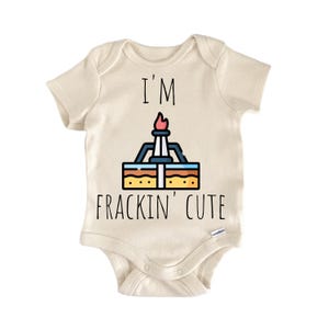 May include: Cream-colored baby onesie with the text "I'M FRACKIN' CUTE" in black. The onesie features a colorful graphic of an oil derrick with a flame at the top. The design is centered on the front of the garment.