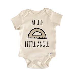 May include: A cream-colored short-sleeve baby bodysuit featuring a black graphic of a protractor and the text ACUTE LITTLE ANGLE printed in black. The garment has a round neckline and snap closures at the bottom for easy access and secure fastening.