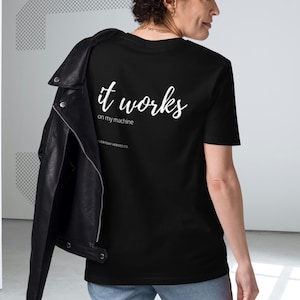 Puede incluir: Camiseta negra con la frase "it works" en escritura blanca en la espalda. La frase "on my machine" está debajo. Una chaqueta de cuero negra está sobre los hombros. Una prenda de vestir casual.