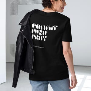 May include: Black t-shirt with the words "Commit, Push, Pray" in white, arched text on the back. The shirt also has the text "Everyday Heroes Co." below the main text. A black leather jacket is draped over the shoulders.