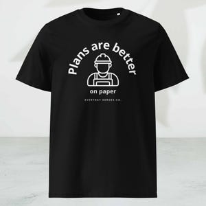 May include: Black t-shirt with white text and a graphic of a construction worker. The text reads "Plans are better on paper" with "Everyday Heroes Co." below. The shirt is a crew neck.