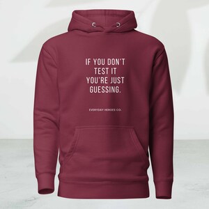 Può includere: Una felpa con cappuccio bordeaux con tasca frontale e cappuccio con coulisse. La parte anteriore della felpa presenta il testo "IF YOU DON'T TEST IT YOU'RE JUST GUESSING." e il marchio "EVERYDAY HEROES CO."